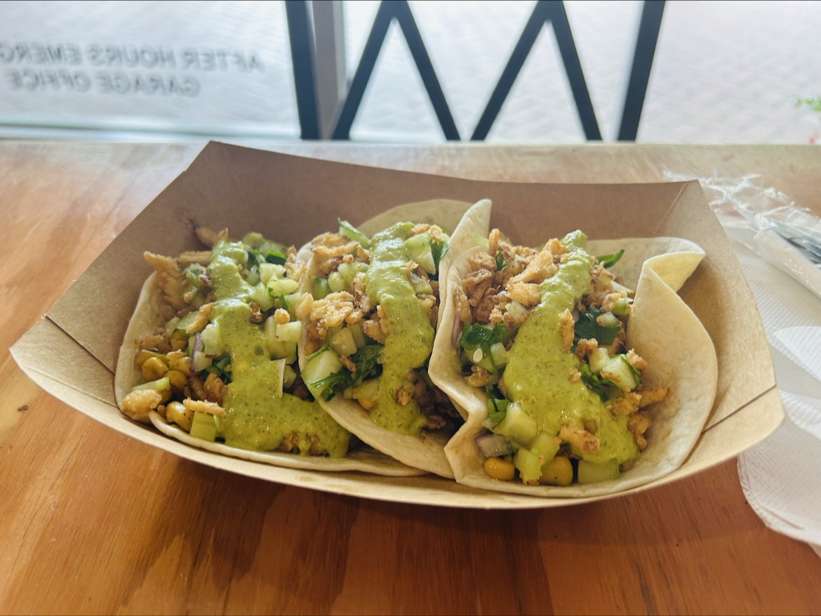Three tacos with green sauce in a takeout boat
