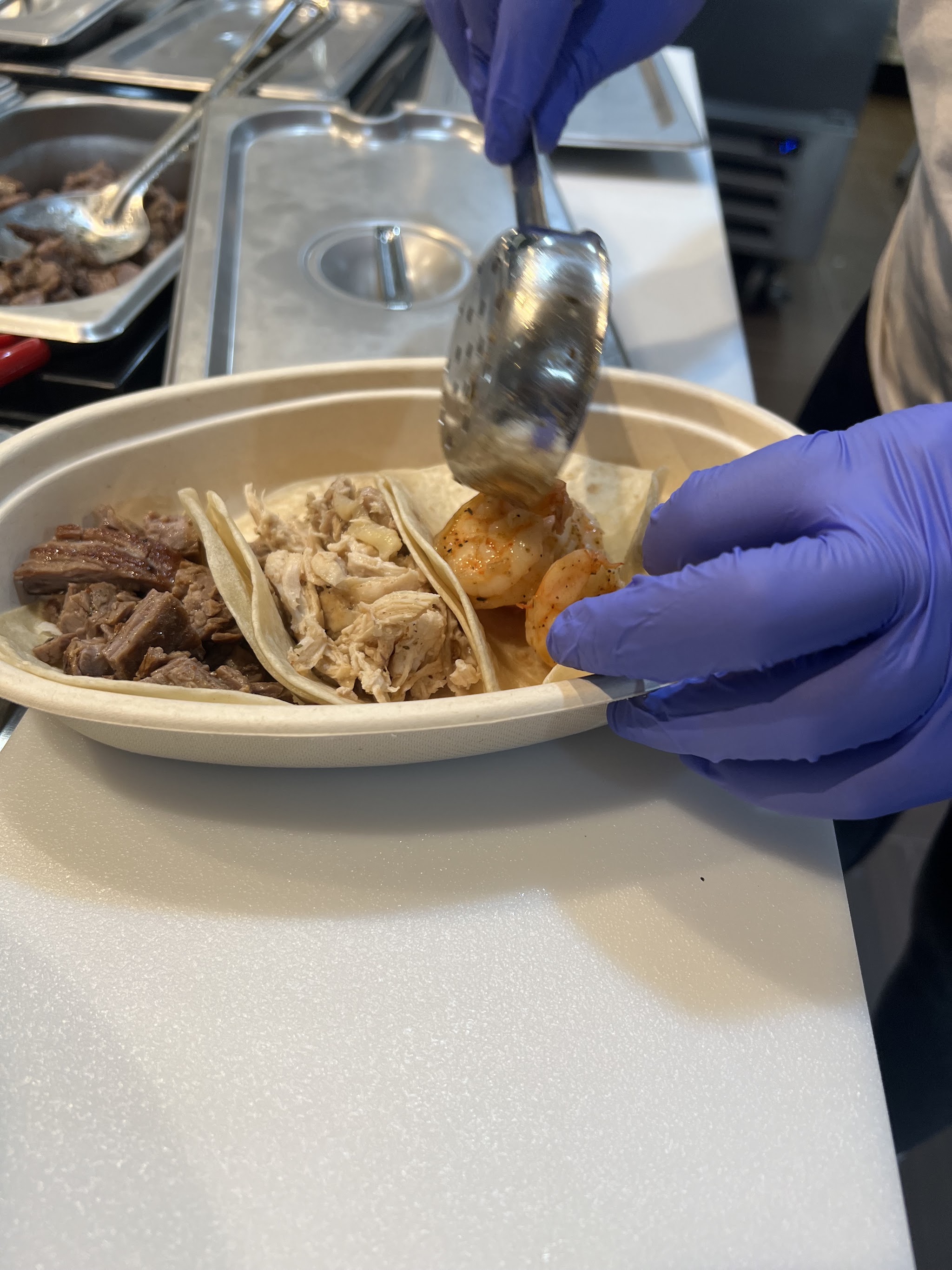 Staff plating a tray of steak, chicken and shrimp tacos